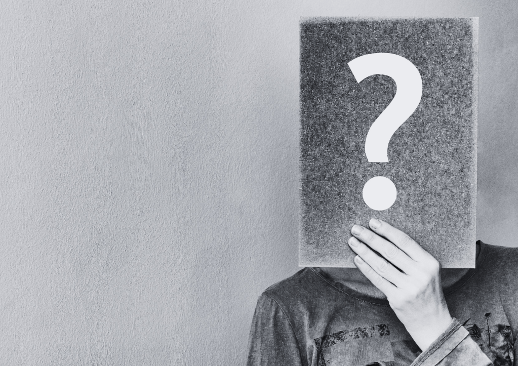 une personne au visage masqué derrière une pancarte avec un point d'interrogation