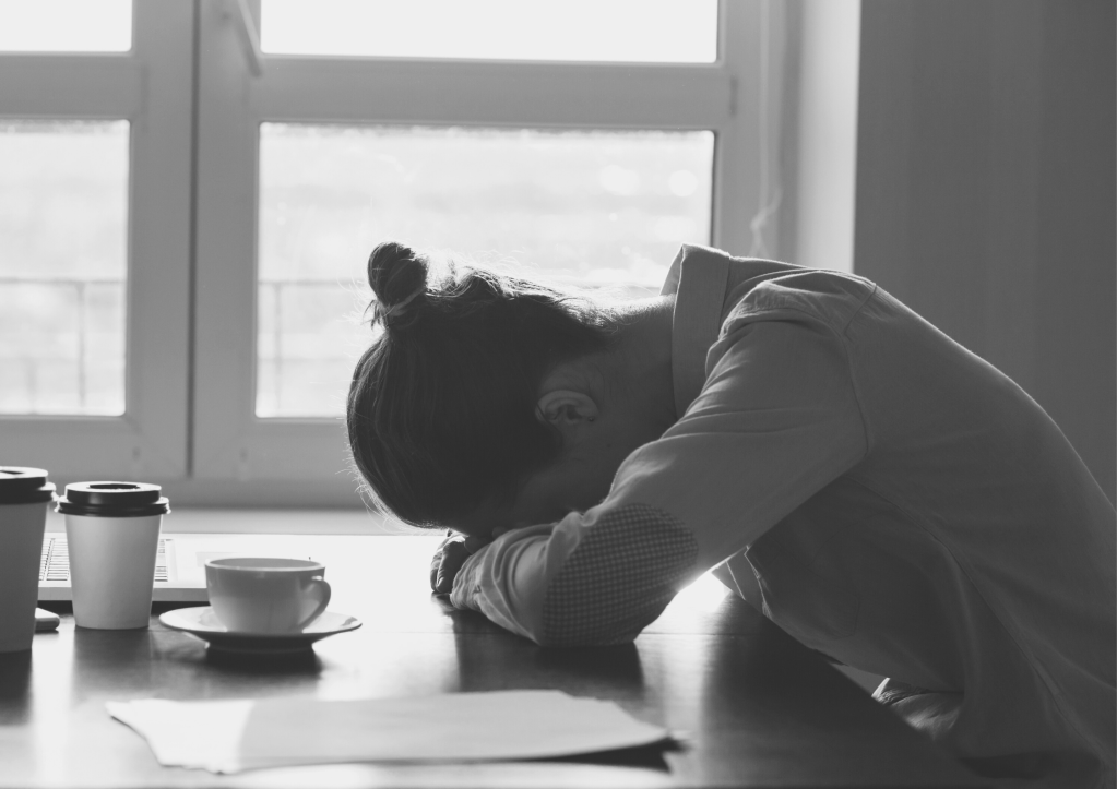 une femme a replié ses bras sur sa table pour y poser la tête devant sa tasse de café