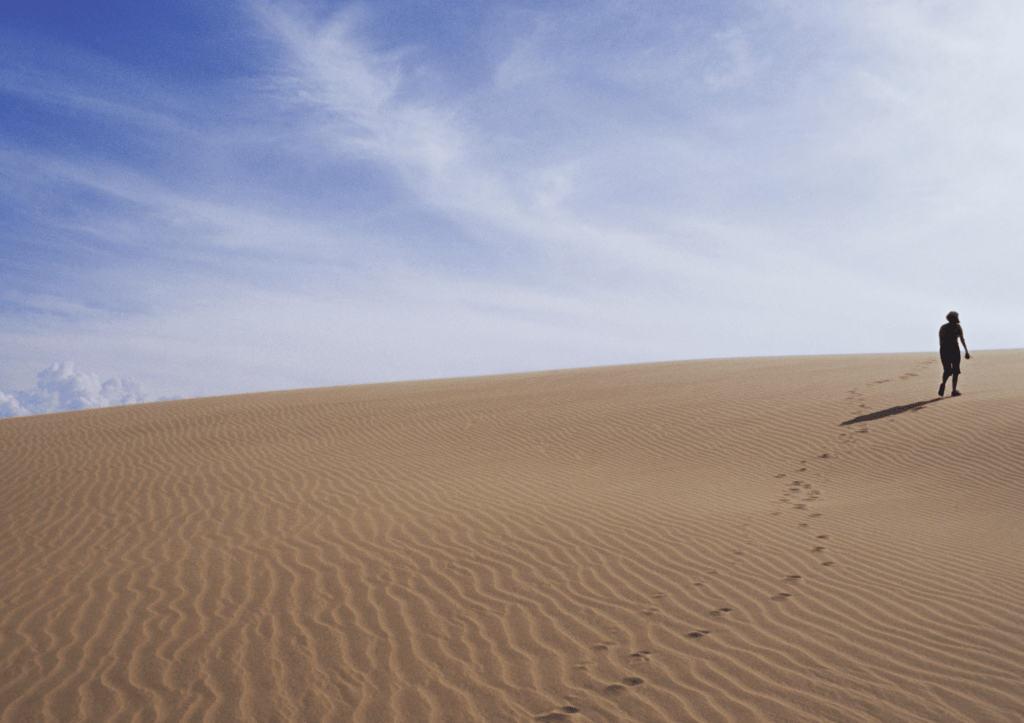 désert sous un ciel bleu, une personne marche au loin et a laissé des traces de pas 